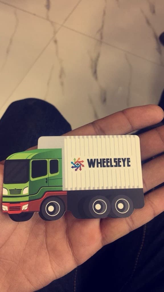 A WheelsEye truck-shaped business card held in a hand, showing the brand side with logo on the trailer