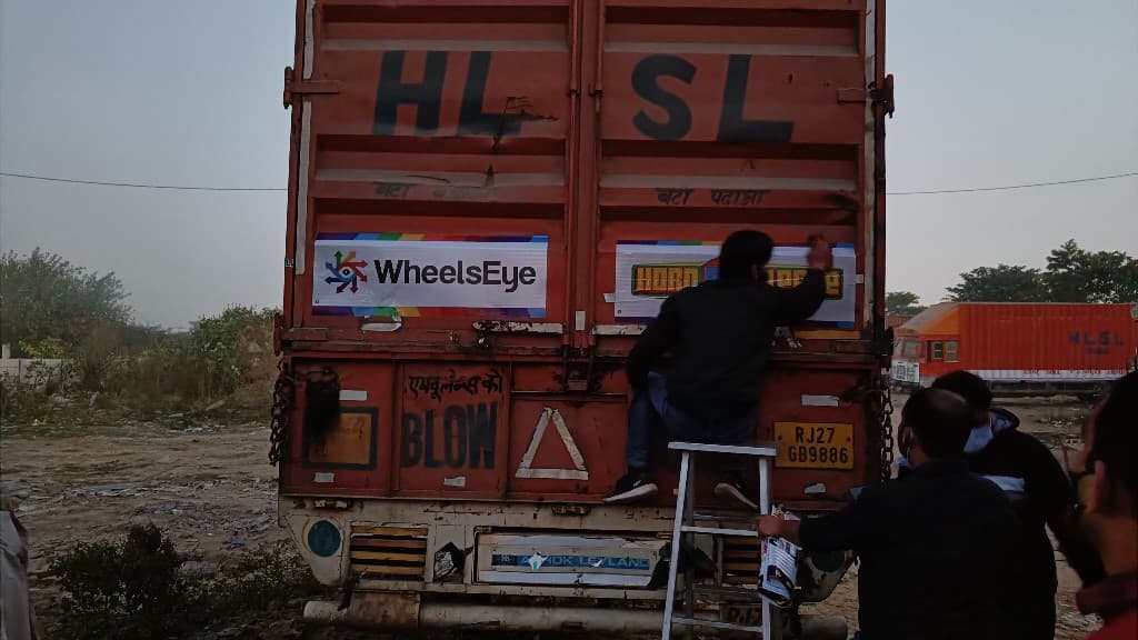 A field team member on a ladder applying a WheelsEye sticker to the back of a truck