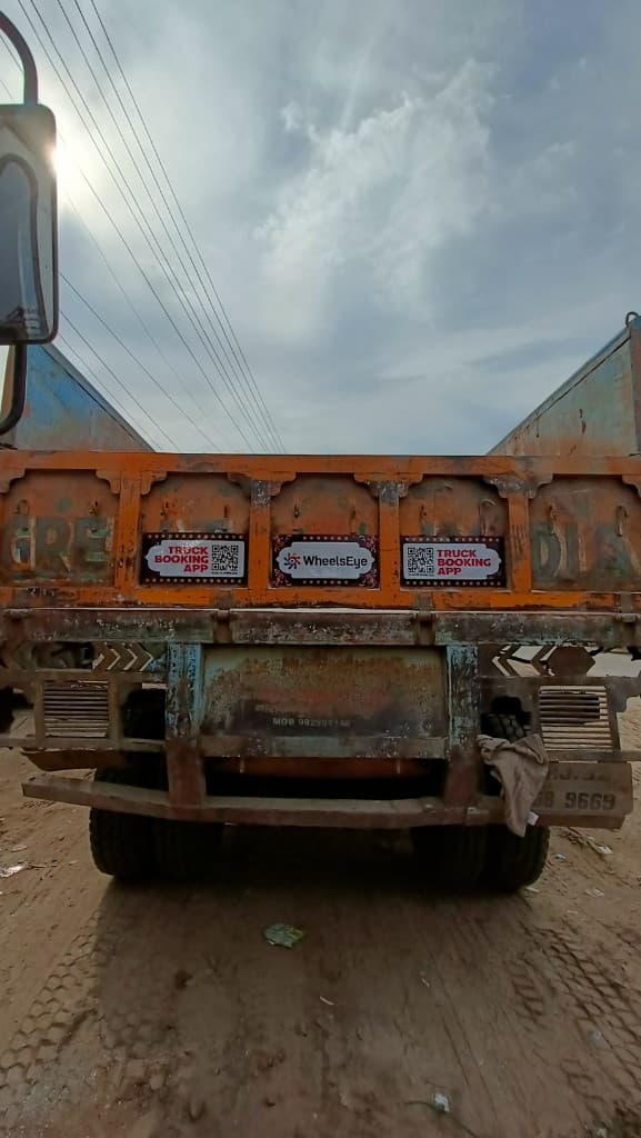 An orange truck with WheelsEye logo and truck booking app QR code stickers on the tailgate